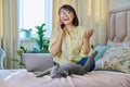Middle-aged woman sitting on bed with laptop, cat talking on phone Royalty Free Stock Photo