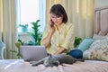 Middle-aged woman sitting on bed with laptop, cat talking on phone Royalty Free Stock Photo