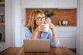 Smiling mid aged woman drinking tea and using laptop at home Royalty Free Stock Photo