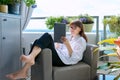 Middle-aged woman sitting at home in chair using digital tablet Royalty Free Stock Photo