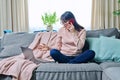 Middle-aged woman sitting at home on sofa, looking in laptop, talking on phone Royalty Free Stock Photo