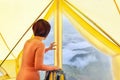 Middle aged woman sitting inside yellow tent looking at valley