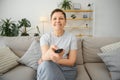 middle-aged woman sitting on the sofa and turning on the TV with a remote control. Royalty Free Stock Photo