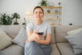 middle-aged woman sitting on the sofa and turning on the TV with a remote control. Royalty Free Stock Photo