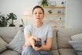 middle-aged woman sitting on the sofa and turning on the TV with a remote control. Royalty Free Stock Photo