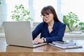 Middle aged woman sitting at workplace in home office, holding pet parrot on shoulder Royalty Free Stock Photo