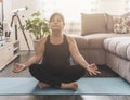 Middle aged woman sitting in yoga position with closed eyes - Senior woman relaxes meditating in her home - Healthy life and