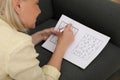 Middle aged woman solving sudoku puzzle on sofa at home Royalty Free Stock Photo