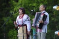 Middle-aged woman in Ukrainian traditional embroidery costumes singing on stage, accordionist playing