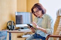 Middle aged woman using smartphone sitting in armchair in home office Royalty Free Stock Photo