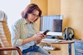 Middle aged woman using smartphone sitting in armchair in home office Royalty Free Stock Photo