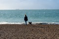 A middle aged woman walking her black dog along a pebble beach with the sea in the background Royalty Free Stock Photo