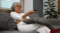 Middle aged woman watching tv on comfortable sofa, enjoying carefree leisure weekend activity at home Royalty Free Stock Photo