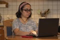 A middle-aged woman wearing glasses works on a laptop at her home kitchen table. Royalty Free Stock Photo