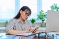 Middle aged woman working with computer, using smartphone, in home office Royalty Free Stock Photo