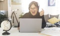 Middle-aged woman works at home computer - woman in video call with headphones