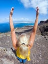 Middle-aged woman in yellow t-shirt and jeans raising her arms to the sky on top of a cliff Royalty Free Stock Photo