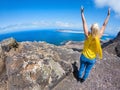 Middle-aged woman in yellow t-shirt and jeans raising her arms to the sky on top of a cliff on a sunny day Royalty Free Stock Photo