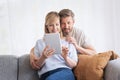 Happy mid aged couple relaxing on the sofa at home and using touchpad Royalty Free Stock Photo