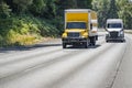 Middle and big rigs semi trucks with trailers transporting cargo running side by side on the turning highway road in green forest Royalty Free Stock Photo