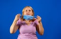Middle blonde woman taking off her medical mask isolated on blue background