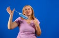 Middle blonde woman taking off her medical mask isolated on blue background