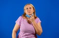 Middle blonde woman taking off her medical mask isolated on blue background