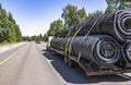 Day cab white big rig semi truck transporting plastic pipes on the long flat bed semi trailer driving on the narrow highway road Royalty Free Stock Photo