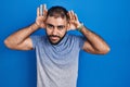 Middle east man with beard standing over blue background trying to hear both hands on ear gesture, curious for gossip Royalty Free Stock Photo