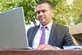 Middle eastern man is typing on a laptop. Serious young man in business suit and tie works on open veranda