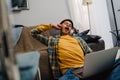 Teenage boy yawning while using laptop and sitting on floor at home