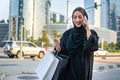 Middle eastern young woman with shopping bags talking on mobile phone on the city street. Royalty Free Stock Photo