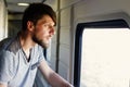 Middle plane portrait of a handsome young caucasian man with a beard, looks outside of the train`s window