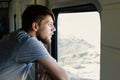 Middle plane portrait of a handsome young caucasian man with a beard, looks outside of the train`s window