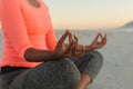 Middle section of mixed race woman on beach practicing yoga meditating