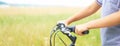 Middle section of teenage boy who holds the handlebar of a bicycle and rides along the road next to the field. Royalty Free Stock Photo