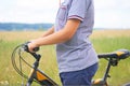 Middle section of teenage boy who holds the handlebar of a bicycle and rides along the road next to the field. Royalty Free Stock Photo