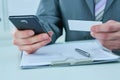 Middle section of young businessman dials a number on the phonewhile holding business card at workplace.