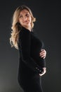 Middle selection on pregnant woman puts hands on her belly. Female in black bodycon dress.black Background Royalty Free Stock Photo