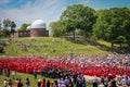 Looking down on graduates and crowd sitting in seats and on the ground for graduation ceremony with