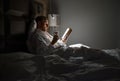 Midle-aged man relaxing rin bed reading book holding a glass of red wine with bedside lamp turned on. Evening relaxation, hobbies Royalty Free Stock Photo