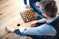 A midsection of adult son and senior father sitting on floor indoors, playing chess.