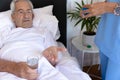 Midsection of biracial female physiotherapist giving medicines to caucasian senior man lying on bed Royalty Free Stock Photo