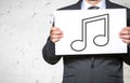 Midsection of businessman holding placard with music note sign while standing against white brick wall Royalty Free Stock Photo