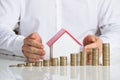 Businessman Protecting House Model With Stacked Coins At Desk Royalty Free Stock Photo