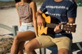 Midsection of caucasian couple sitting on beach by the sea playing guitar