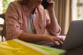 Midsection of caucasian woman sitting working in living room, using laptop and talking on smartphone Royalty Free Stock Photo