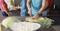 Midsection of diverse group of friends preapring meal, chopping vegetables in kitchen, slow motion