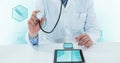 Midsection of doctor using stethoscope with digital tablet and mobile phone on desk