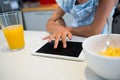 Midsection of girl using digital tablet by breakfast on kitchen counter